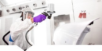 Male painter spraying primer on a car part using 3M spray gun
