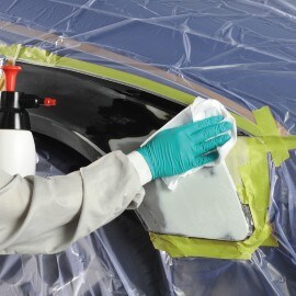 A hand with a green glove degreasing a car body part with a white wipe