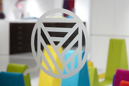 Clear glass window with etched glass-style line art logo with colorful shapes behind.
