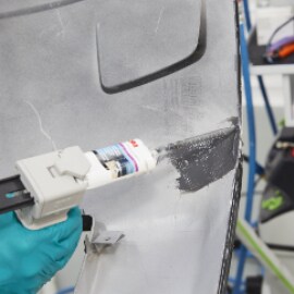 Using a manual gun to apply flexible repair material onto the backside of the crack