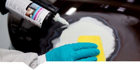 Technician applying filler to damaged car panel
