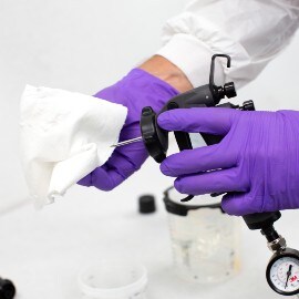 Hands with purple gloves cleaning a spray gun needle with a white wipe