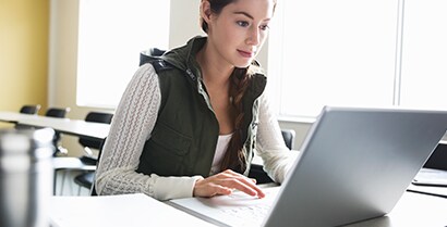 A student works on a laptop near a bright sunny window not worrying about glare on her screen
