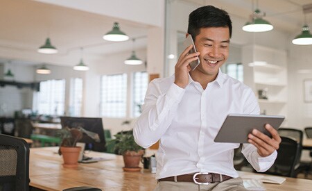 Image of smiling businessman talking on phone and looking at tablet.
