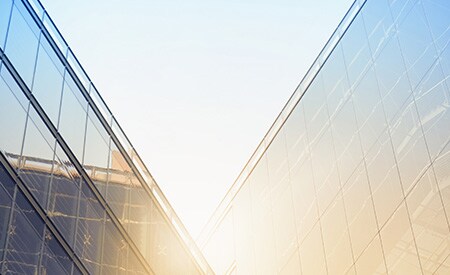 Bright sun shining over angular window-covered buildings
