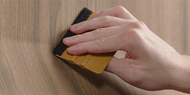 Closeup of squeegee tool being used to install wood pattern film
