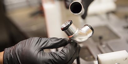 Learn about material bonding. Image of a metal pipe with adhesive about to be joint with a metal elbow joint.
