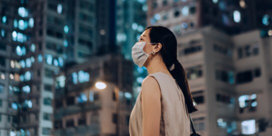 woman in mask standing in a city at night - 3M state of science index global 2022 report
