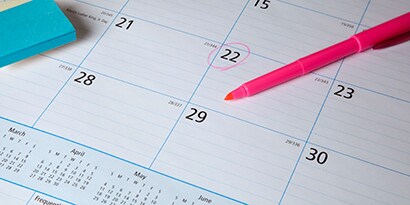 Post-it® notes and a pink highlighter on top of a desk calendar one of the dates is circled
