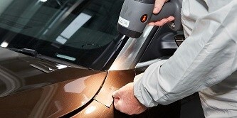Man comparing a colour sample card with a car paint area using the 3M Colour check Light II 
